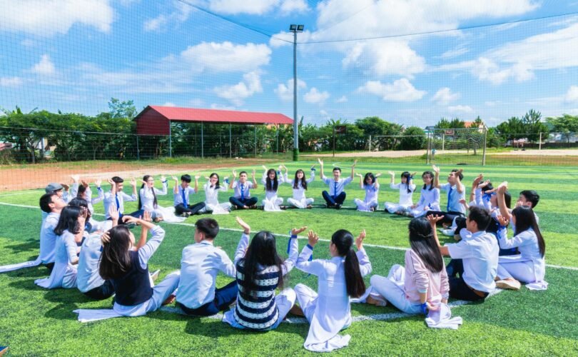 people sitting on green lawn grass while doing hands up at daytime